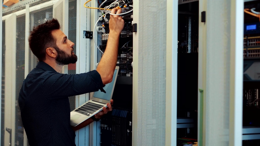 IT Technician Works With Ware And Cables in Big Data Center. Connecting Lan Cable To Mainframe.IT Engineer Patching Network Equipment In Server Room. Network Engineer Maintenance Work In Server Room Royalty-Free Stock Footage #1070468950