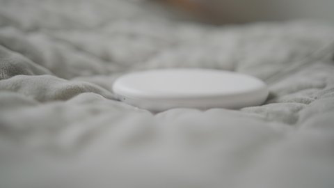 Close-up of a woman's hand placing a smartphone on a wireless charging device on the bed.