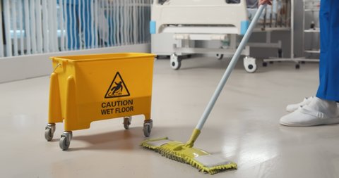 Close up of janitor washing floor with mop and bucket in hospital ward. Cropped shot of nurse or cleaning staff mopping floor in clinic. Healthcare and hygiene concept