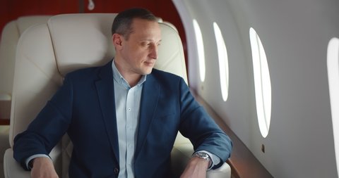 Businessman in suit on business trip by first class flight. Mature executive relaxing in private jet and looking out of window enjoying travelling