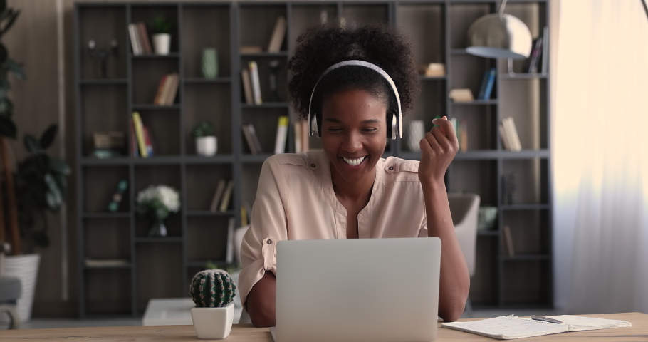 Smiling young 25s mixed race african woman in headphones enjoying remote virtual event, talking by video call computer application with colleagues, friends or clients, distant communication concept. Royalty-Free Stock Footage #1070476432