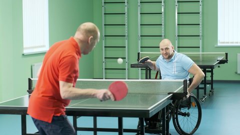 A man who uses a wheelchair plays ping pong. People with disabilities play table tennis. Rehabilitation of the disabled. Paralympic sport.
