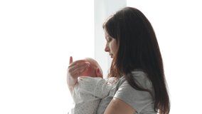 Happy mother holding her baby while standing by the window. High quality 4k footage