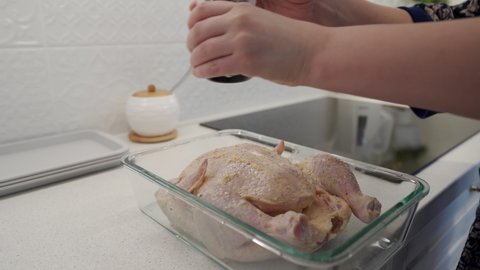 Woman cooking whole baked chicken in the kitchen, sprinkling with ground pepper, using a pepper mill. High quality 4k footage