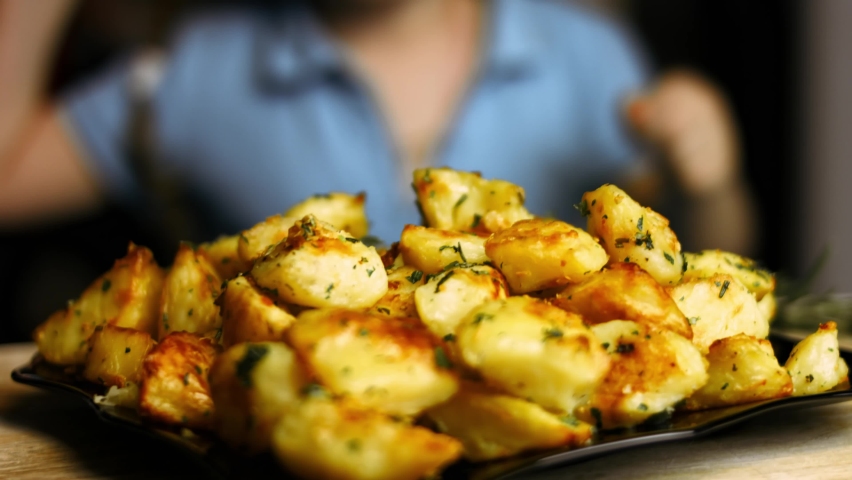 Beautiful blonde 5 y.o. girl eating roasted golden potatoes spiced with fried garlic and rosemary and fresh parsley on a plate. Process of cooking perfect oven roasted potatoes
