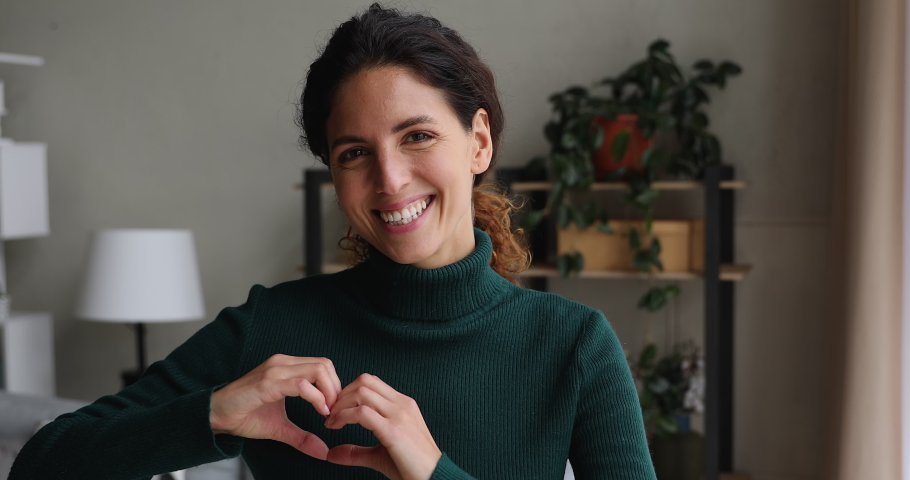 Sincere kind beautiful millennial european woman looking at camera, showing heart symbol, expressing love and support indoors, feeling affection. Candid female volunteer demonstrating donation sign. | Shutterstock HD Video #1070487817