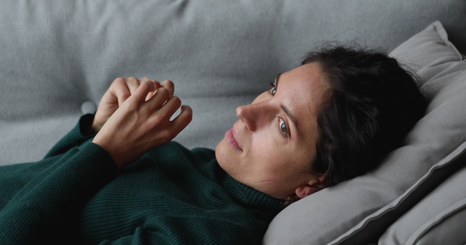 Side view anxious young woman lying on pillow on sofa, feeling doubtful making difficult decision. Nervous millennial lady suffering from negative thoughts, unwanted pregnancy, relationship problems. Royalty-Free Stock Footage #1070487883