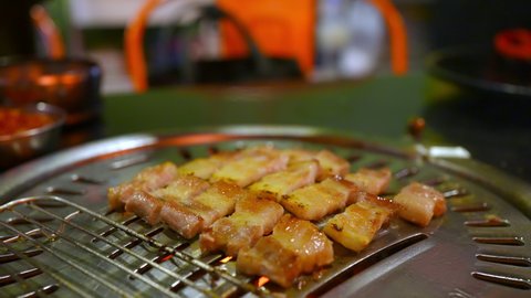 Chef hand cooking grilled pork belly meat on iron BBQ grill pan for dinner in Korean restaurant. Traditional delicious Korea style food barbecue pork steak on charcoal grill. Food and business concept