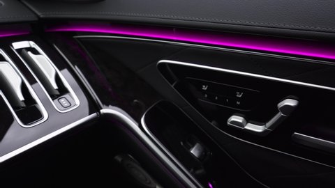 Interior of a luxury new premium car. Close-up of the car door with wood trim and pink LED lighting, electric adjustment of the seats, power windows.