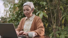 Senior business woman using his laptop while drinking his coffee. Senior business woman in coffee shop using his laptop and drinking his coffee. Close up footage of Senior business woman using laptop. - Powered by Shutterstock - Get 15% off with code: PIKWIZARD15