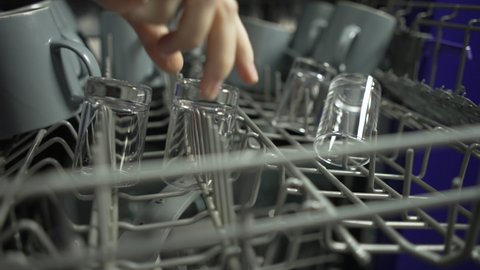 Female hand pulls clean glasses out of the dishwasher. The housewife does the housework of washing dishes.