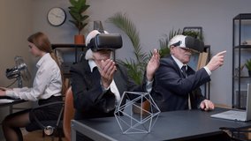 Senior business colleagues using VR app headset helmet doing research. Elderly people watching virtual reality 3D 360 video graph simulation at office. Busy freelancers working on modern tech device