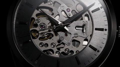 Luxury skeleton swiss watch with full open mechanism rotating and going into the dark. Dramatically flickering light illuminates running gears and arrows