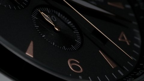 Golden second arrow running on the black clockface of luxury swiss watch with chronograph. Light flash on the turning clockface. Closeup on black background