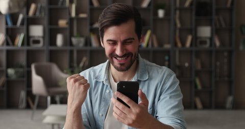 Sincere emotional young handsome man looking at cellphone screen, feeling excited of getting message with amazing news, celebrating betting auction online lottery giveaway win, internet success.