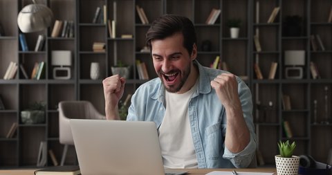 Excited young happy sincere caucasian man looking at laptop screen, feeling amazed by getting email with good news, receiving dream job offer, bank loan mortgage approvement or online lottery win.