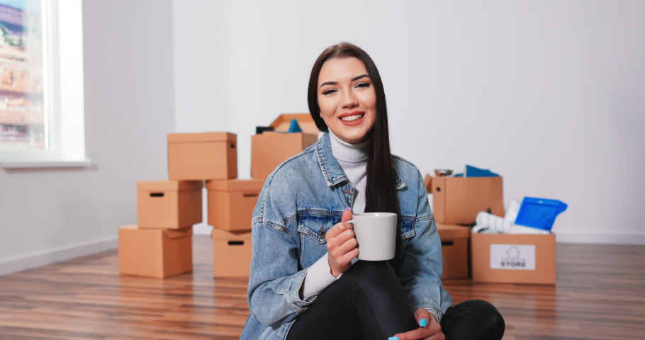 Cheerful Caucasian woman sitting on floor in living room with cup of coffee and thinkinCheerful Caucasian woman sitting on floor living room with cup of coffee and thinking about new interior