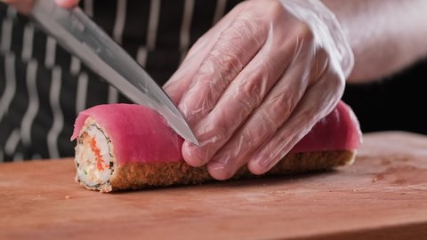 Process of preparing sushi. Chef cutting sushi rolls with sharp knife in japanese restaurant. Close-up of male chef cooking tempura sushi with tuna, shrimp, caviar. 4K, UHD