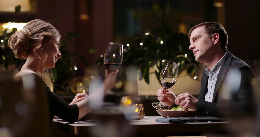 Joyful couple having a romantic dinner at a fancy restaurant. People celebrating their relationship anniversary, saying a toast and drinking wine 4k footage