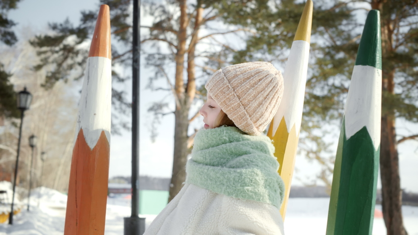 Adorable teenage girl dreaming and looking around in winter park. Portrait of beautiful young girl in winter clothing standing and enjoying nature outdoors at wintertime