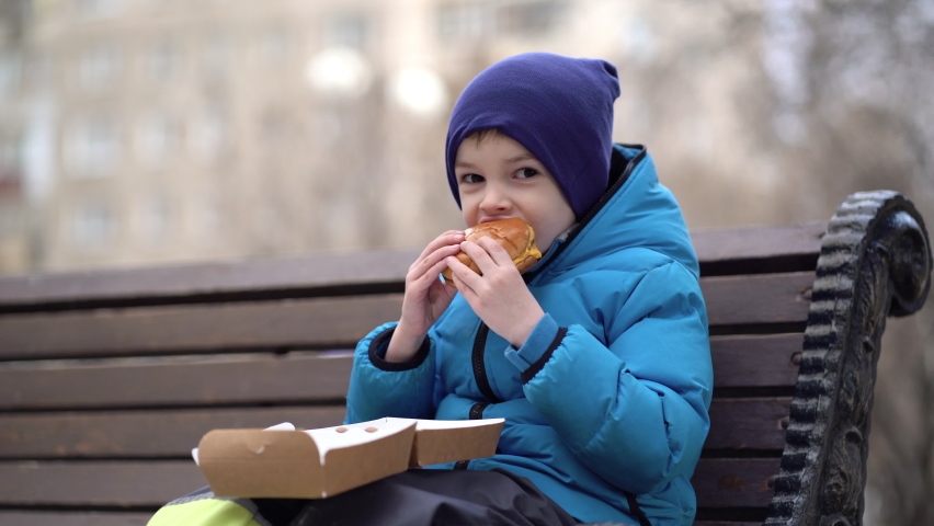 Hungry kid eating double cheeseburger outdoor. Royalty-Free Stock Footage #1070529919