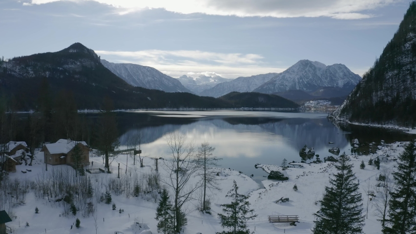 Aerial view moving right shot, Cabin near the lake of grundlsee in Styria, Austria, mountain range reflecting in lake in background.
