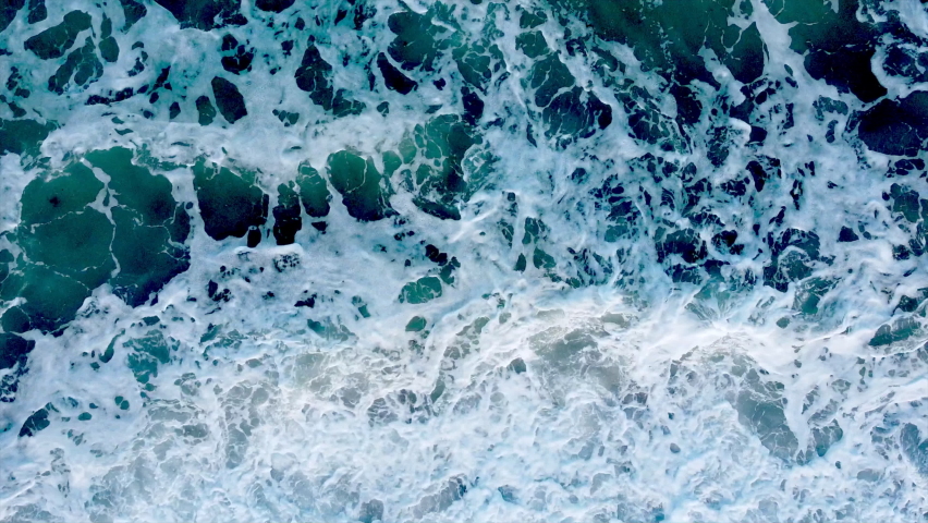 Aerial shot facing down at the oceans shoreline with minimal movement towards the shore.