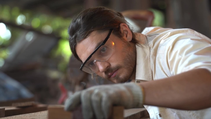 close up face of worker man using sandpaper to rub timber wood at workshop table in carpenter wood factory. Handsome man working on handcraft. Royalty-Free Stock Footage #1070541109