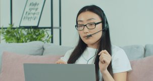 Beautiful Asian woman in glasses video calling on laptop computer, streaming online webinar training, conferencing in distance. Work from home.