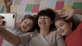 Video Call Family Selfie. Portrait Mother and Kids Kissing on Camera. Happy Mother With Her Kids are Making Selfie or Video Call to Father or Relatives in Bed. Technology, New Generation Parenthood. - Powered by Shutterstock - Get 15% off with code: PIKWIZARD15