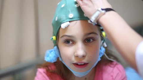 Doctor hands inject electrically-conductive gel into holes in special cap on girl head.
