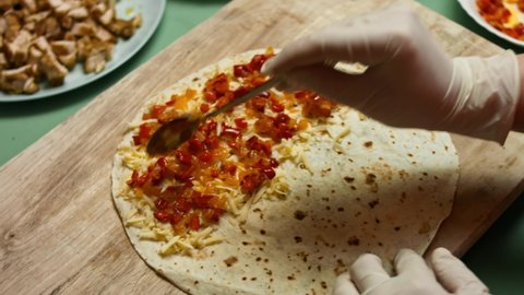 Adding vegetables to flour tortilla filled with grated cheese. Process of making mexican quesadillas with chicken meat, cheese and vegetables. Top view
