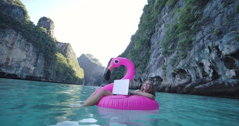 Young freelancer caucasian female floating on inflatable flamingo in the sea, remote working anywhere on her laptop computer connected to office and relax by seeing beautiful view on summer vacation.