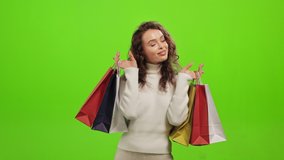 The woman is looking at the camera and smiling. She is raising up the shopping bags. She is standing on a green background. Green screen. 4K - Powered by Shutterstock - Get 15% off with code: PIKWIZARD15
