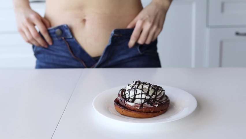 An overweight woman cannot button up her jeans due to the high consumption of sweets