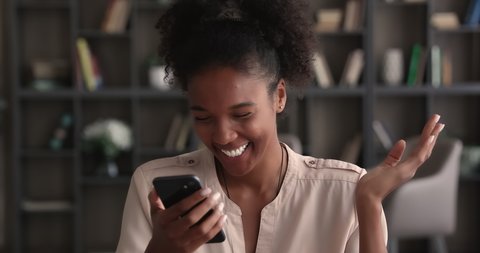 Head shot happy young african american biracial woman looking at cellphone screen, reading message with amazing news, getting dating invitation or online lottery win notification, success concept.