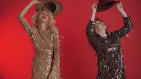 Two cheerful fashionable women wearing sequin dress are dancing at the party. Girls toss their hats up. Celebrating a birthday or new year. Isolated on a red background. - Powered by Shutterstock - Get 15% off with code: PIKWIZARD15