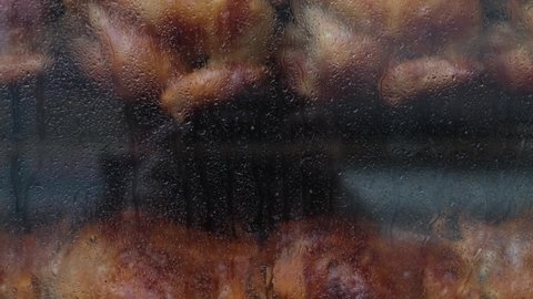 Close-up shot of a steamy rotisserie machine window with water drops. Grilled roasted whole chickens with tasty golden-yellow roasted skin on a turning spit in a row. Restaurant, butcher shop roaster.