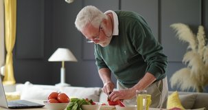Old man chopping vegetables on a chopping board. Retiree's morning routine and breakfast preparation