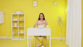 Caucasian woman is looking at camera confidently, having fun in yellow office, playing with marshmallow pieces, throwing them into camera, creative video concept, yellow interior design, Slow motion.