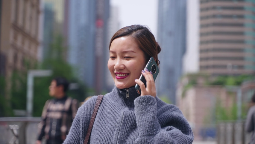 slow motion happy asian woman talking on the mobile phone walking in the sunny urban city street at Chengdu China