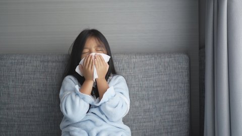 Asian child or kid girl sick and sneezing on nose with cold cough on tissue paper from influenza coronavirus and allergy weak or virus bacteria from PM 2.5 dust weather or smoke at hospital or home 4K