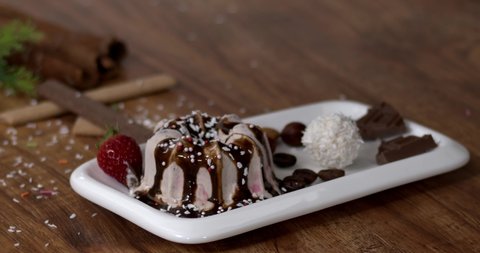 Vanilla ice cream with chocolate and strawberries on a white plate on a wooden table, Waffle and chocolate pods fall slowly on the table. Filmed high speed cinema camera, slow motion, 4K.