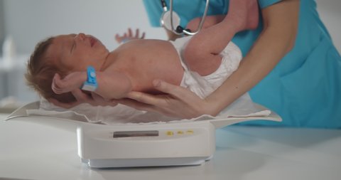 Cropped shot of nurse weighting on scales newborn baby. Pediatrician putting infant on scales doing weight measuring in hospital. Healthcare and medicine concept