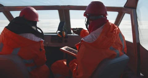 Lifeguards in hovercraft talking on walkie-talkie and using digital tablet navigating in arctic. Professional rescue service team sailing airboat crossing frozen water area in winter