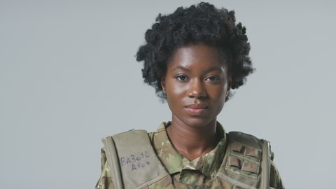 Smiling young female soldier in uniform wearing body armour in front of plain studio background - shot in slow motion