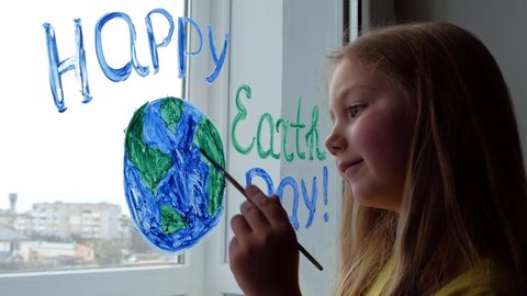 Cute little girl painting planet on window at home 4K. Happy Earth Day April 22 greeting message. Creative family leisure lockdown new reality. Ecology Saving environment conscious consumption concept