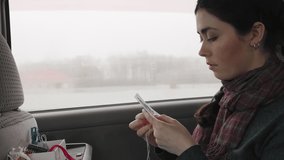 A young woman sits in a car and is engaged in cross-stitch. Side view. Real time.