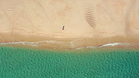 Lingua areia, Portinho da Arrabida, Portugal. Yellowish dunes steeply falling into the calm waters. Aerial view of a tourist running along isolated coastline. High quality 4k footage