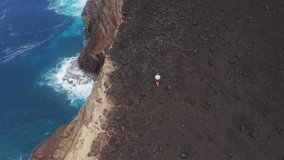 Top view of sportsman exercising on cliff at atlantic ocean, Faial Island, Azores, Portugal, Europe. Aerial view of man running on Capelinhos Volcano surrounded deep ocean waters, 4k footage